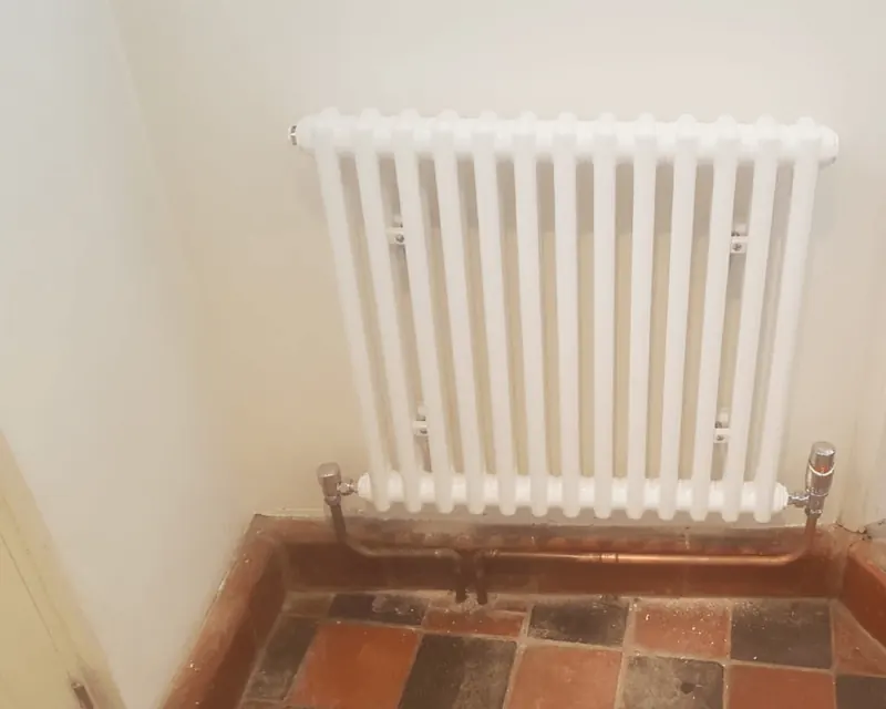 New white column radiator fitted on a tiled hallway floor